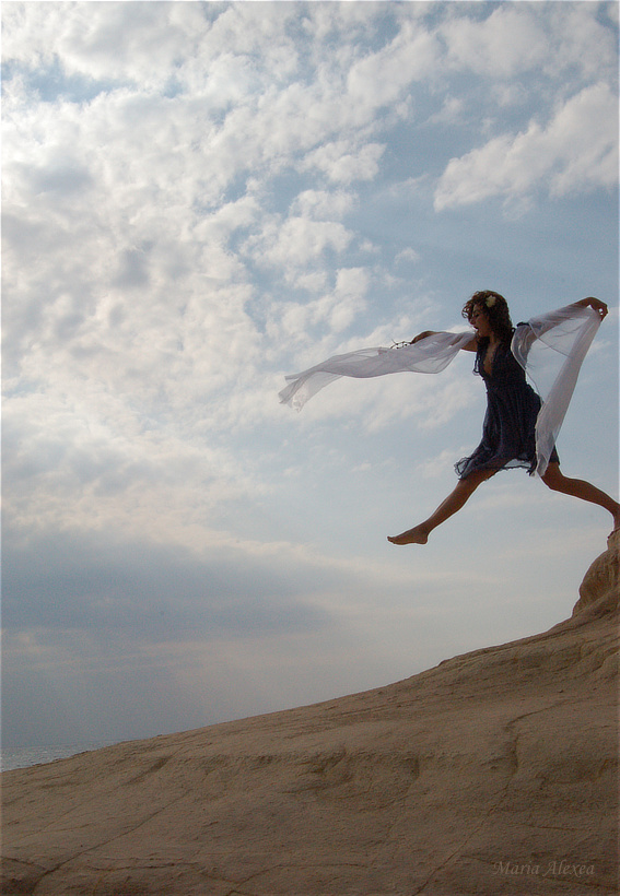 Maria Alexea leaping above a rocky slope beneath a dramatic cloud-filled sky